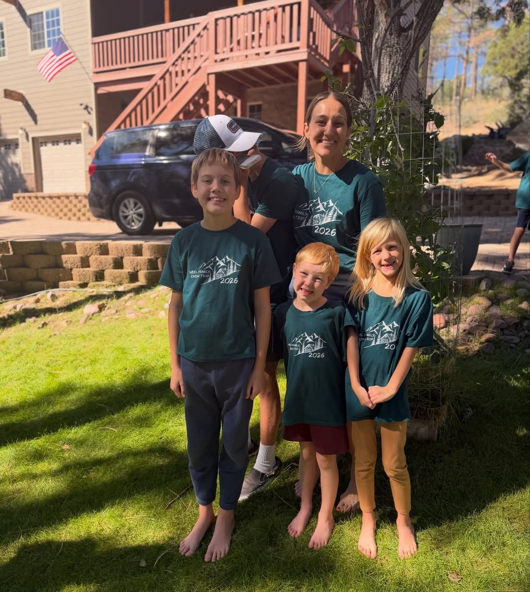 Family of four wearing matching dark green t-shirts posing on a grassy lawn.