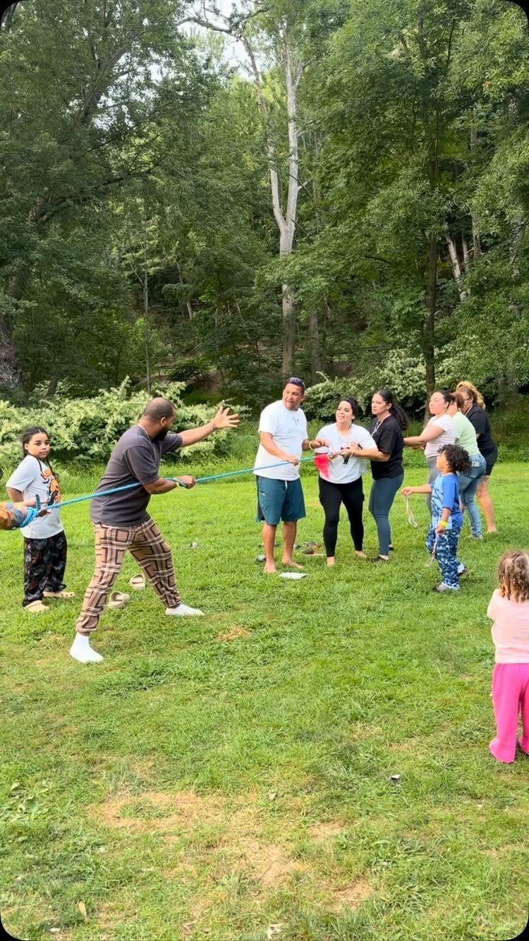 Family members of various ages playing tug-of-war on a grassy lawn outdoors.