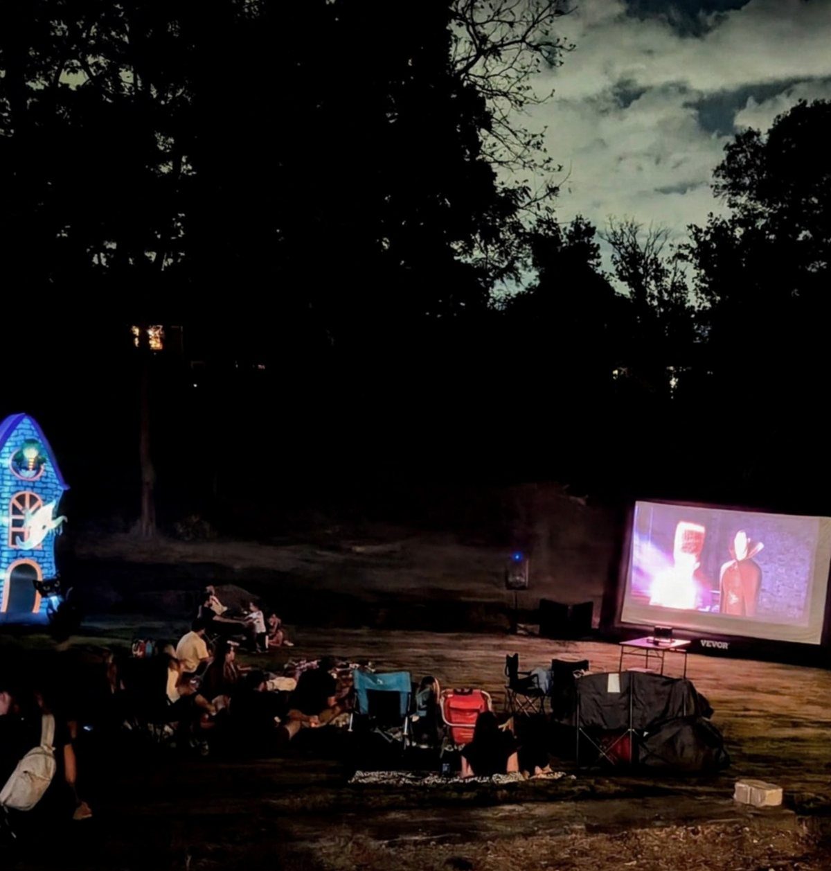 Outdoor movie screen projecting a film for people sitting in lawn chairs at night