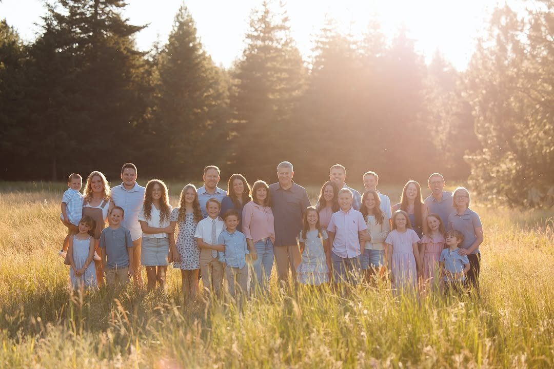 Large multi-generational family posing for a group portrait in a sunny grassy field.