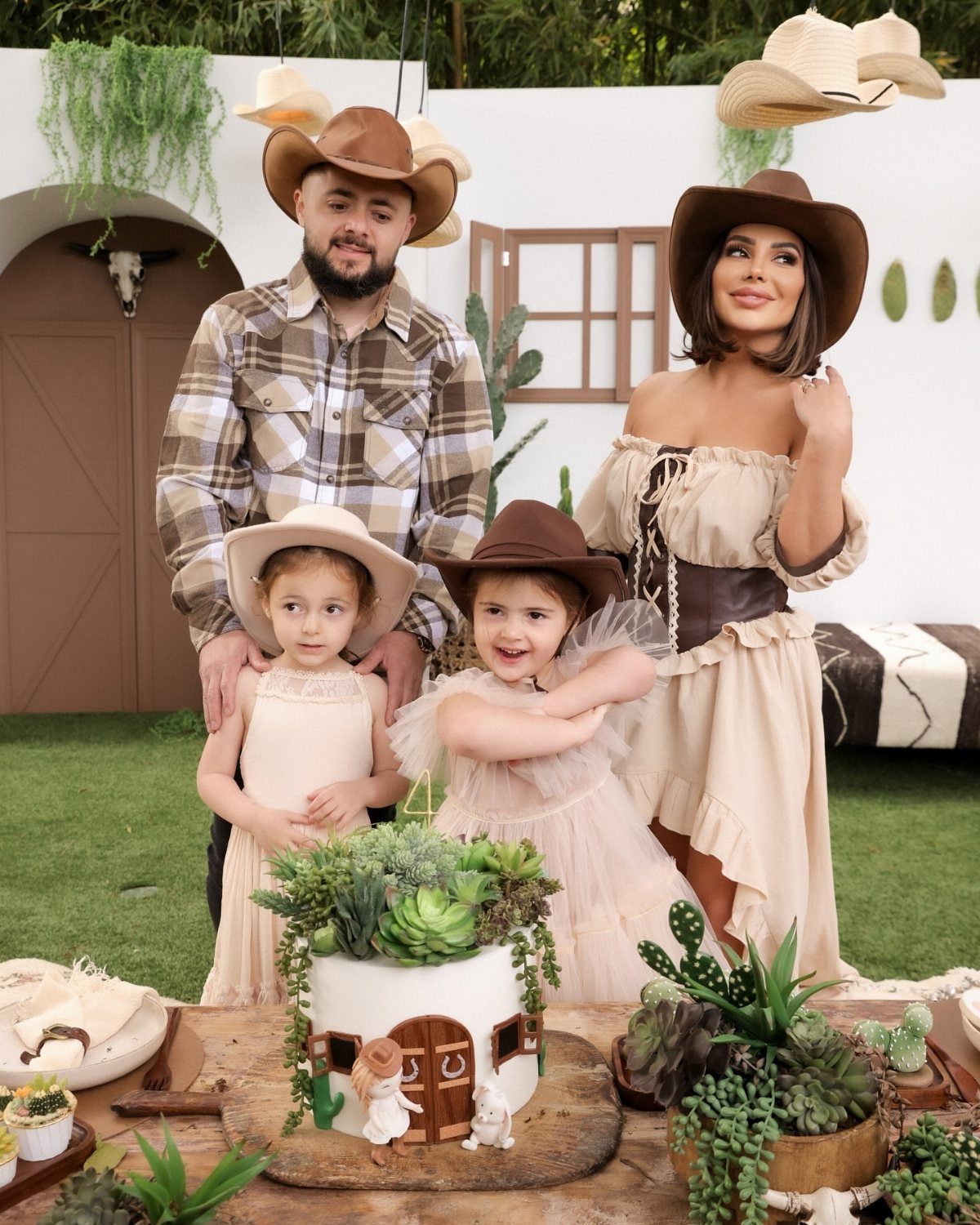 Family of four wearing cowboy hats and Western clothing posing in a themed setting.
