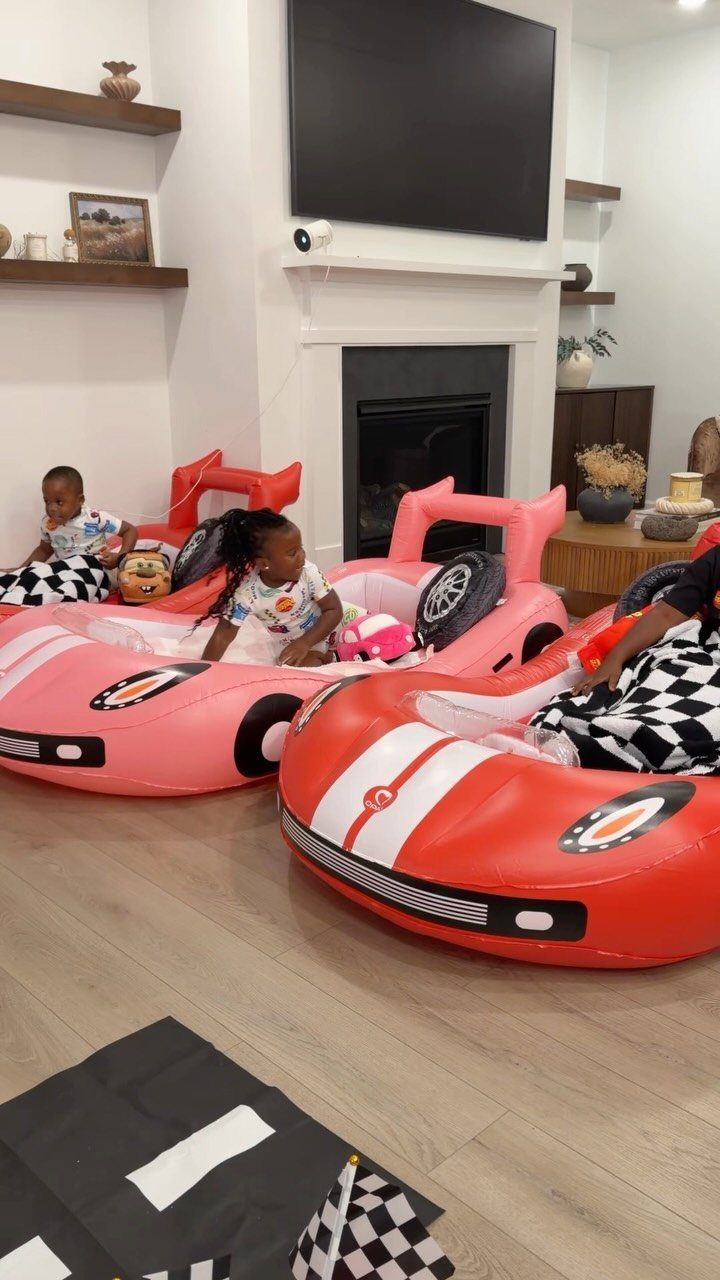 Children sitting in inflatable car seats in a living room facing a television.