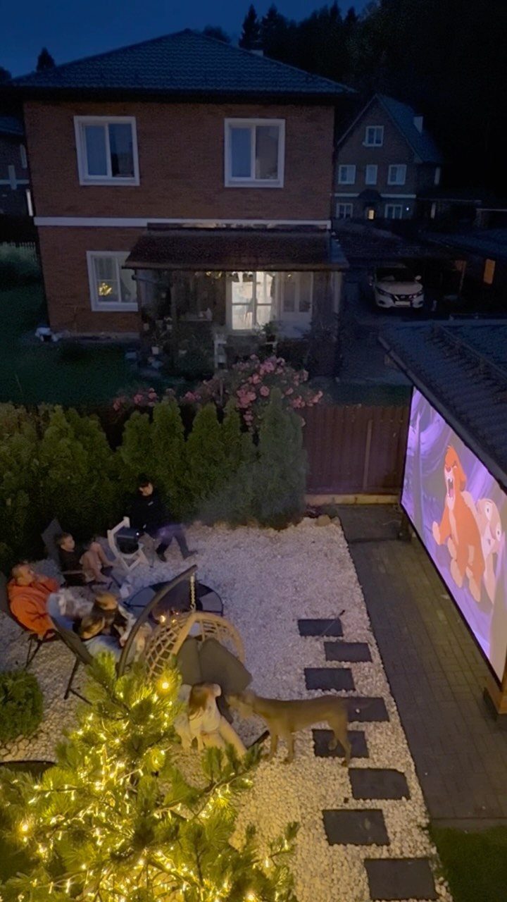 Backyard cinema setup with a large projection screen and people lounging at dusk.