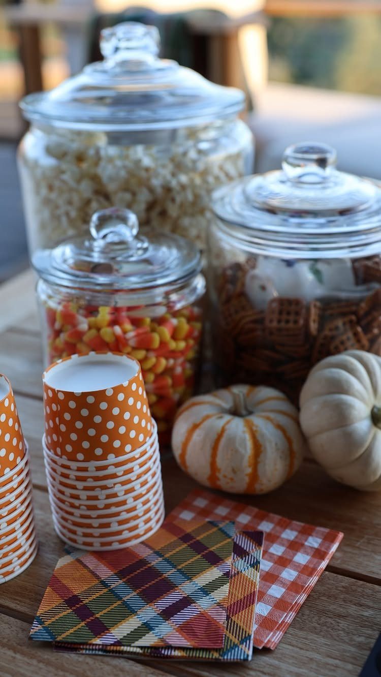 Glass jars of popcorn and candy with pumpkins on a wooden table.
