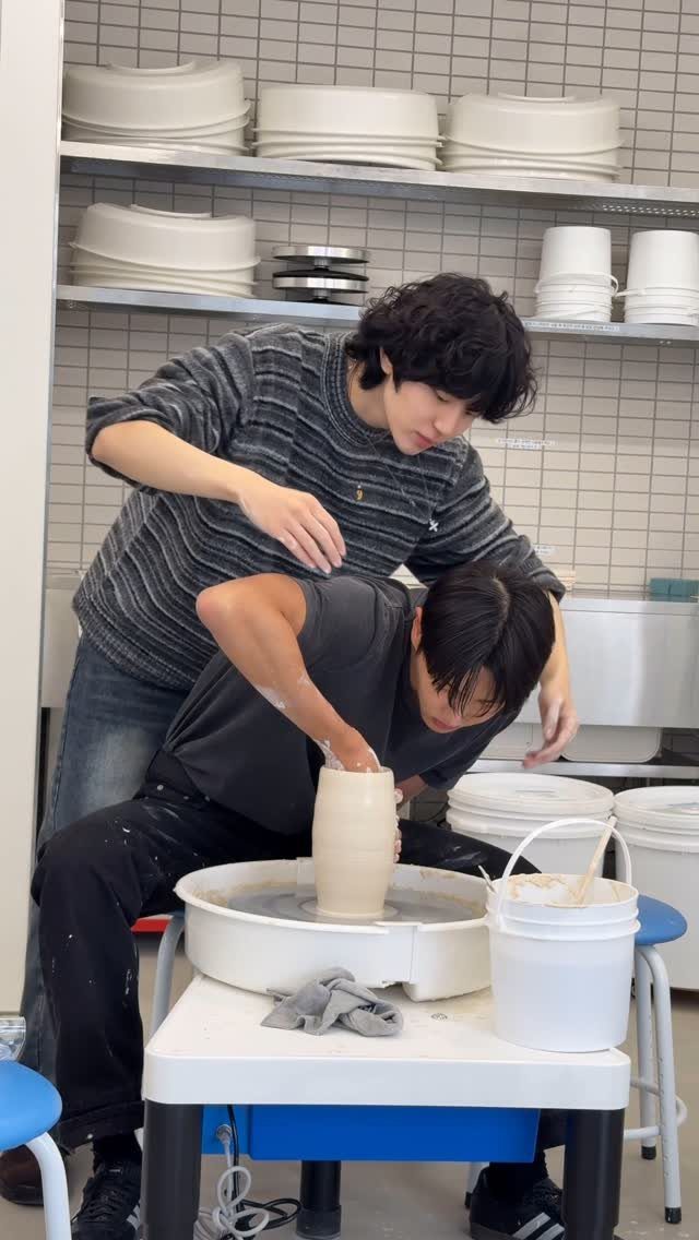 Two men working together to shape a clay vase on a pottery wheel.