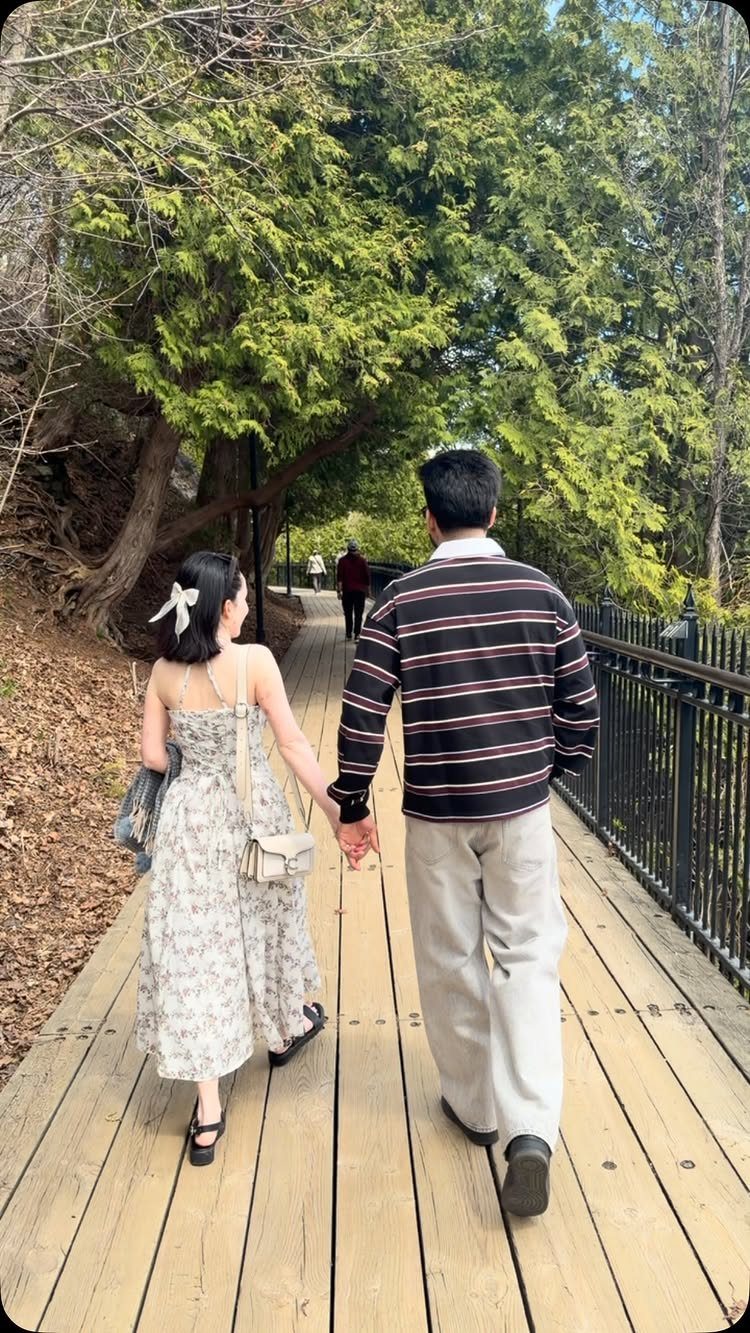 Couple holding hands while walking along a wooden boardwalk through a lush forest