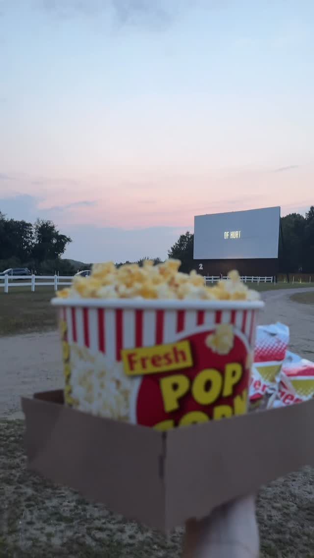 Popcorn bucket in the foreground with a drive-in movie screen at twilight.