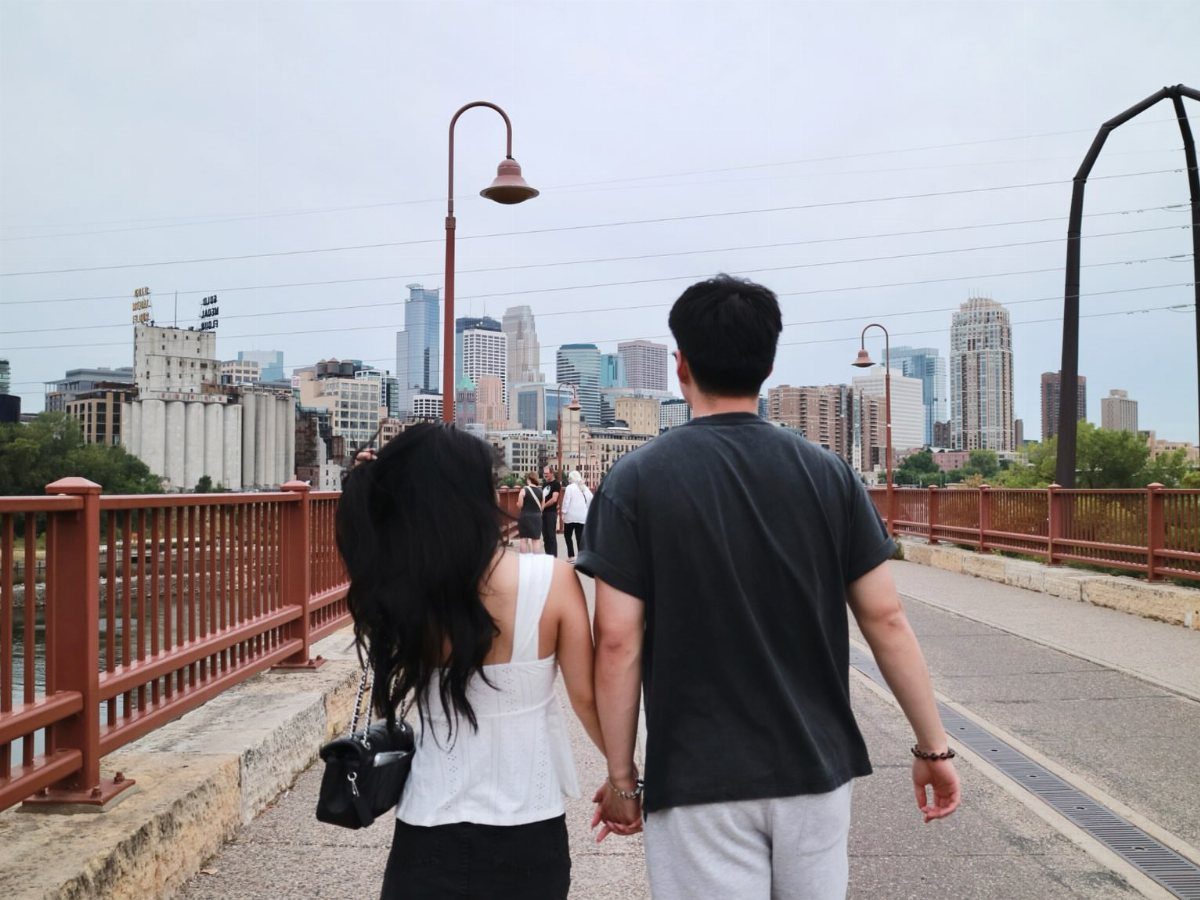 Couple holding hands walking across the Stone Arch Bridge toward the city skyline.