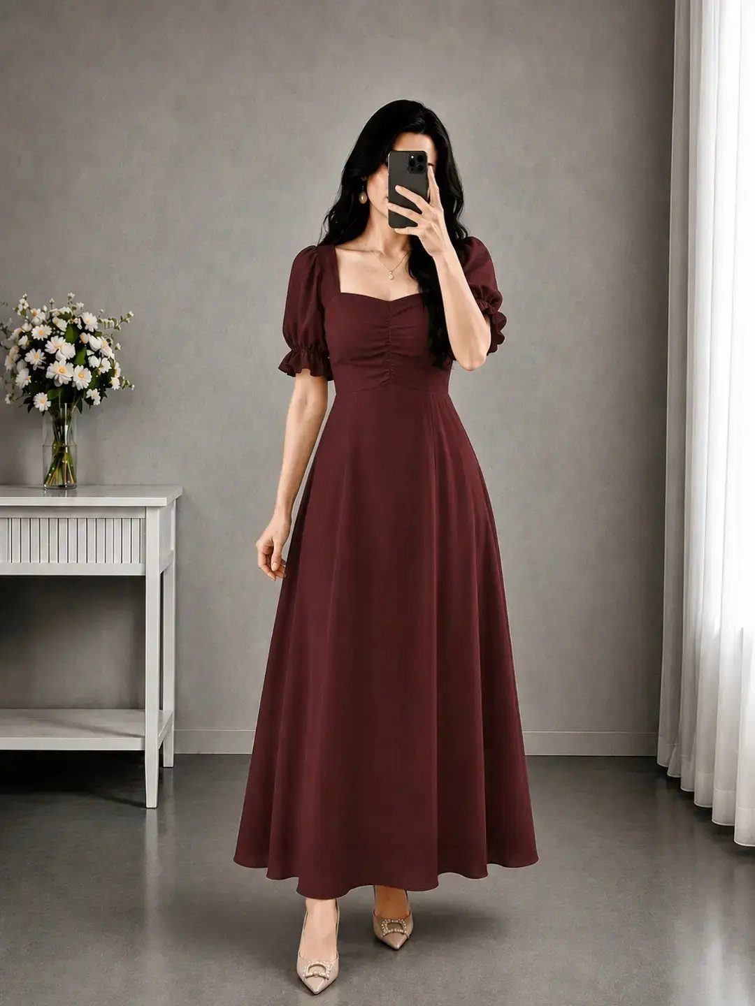 Woman wearing a flowy burgundy maxi dress and nude heels taking a selfie.
