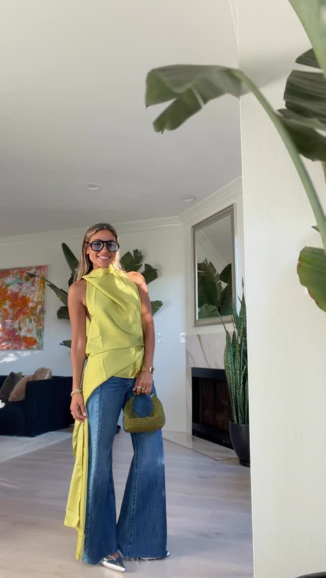 Woman wearing a lime green asymmetrical top and wide-leg blue jeans in a room.