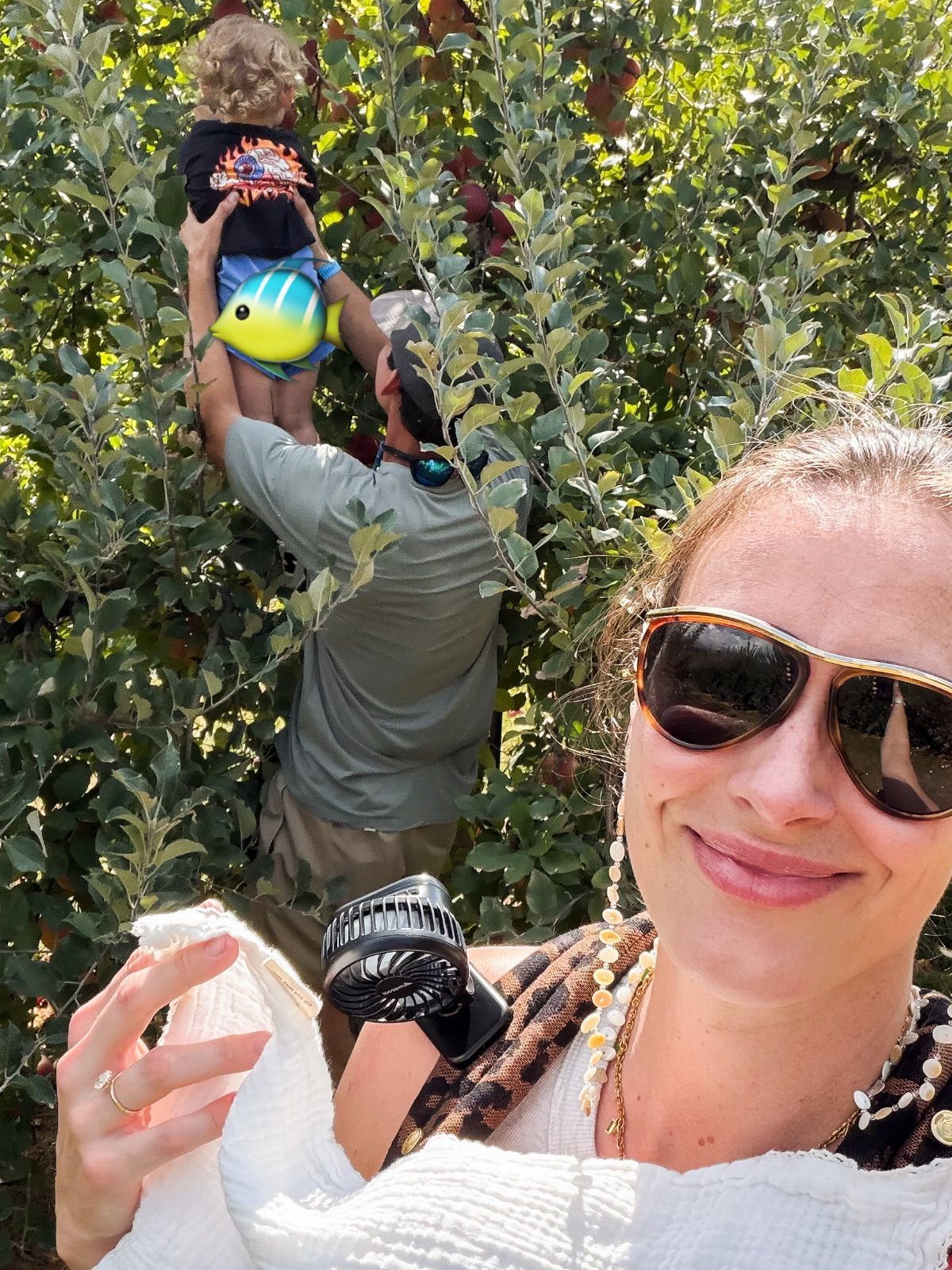 Woman taking a selfie while a man lifts a child in an apple orchard