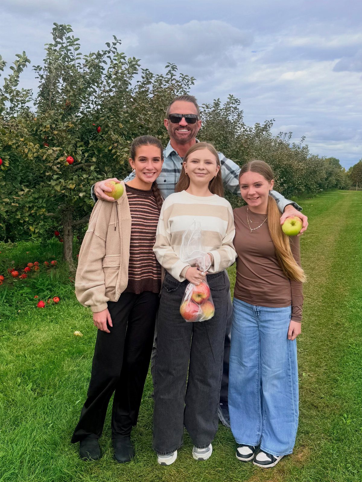 Family of four posing in an apple orchard holding freshly picked apples.