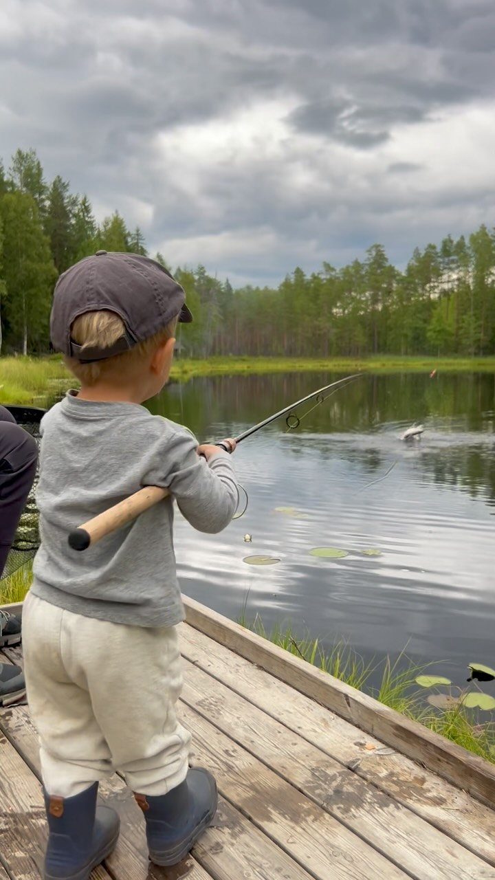 Young child in a cap fishing from a wooden dock on a calm lake