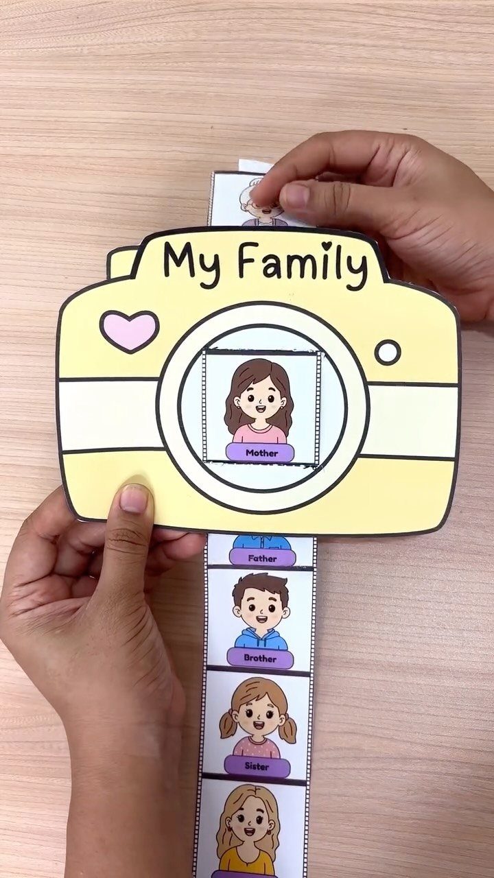 Yellow paper camera craft with sliding cartoon family portraits on a wooden table