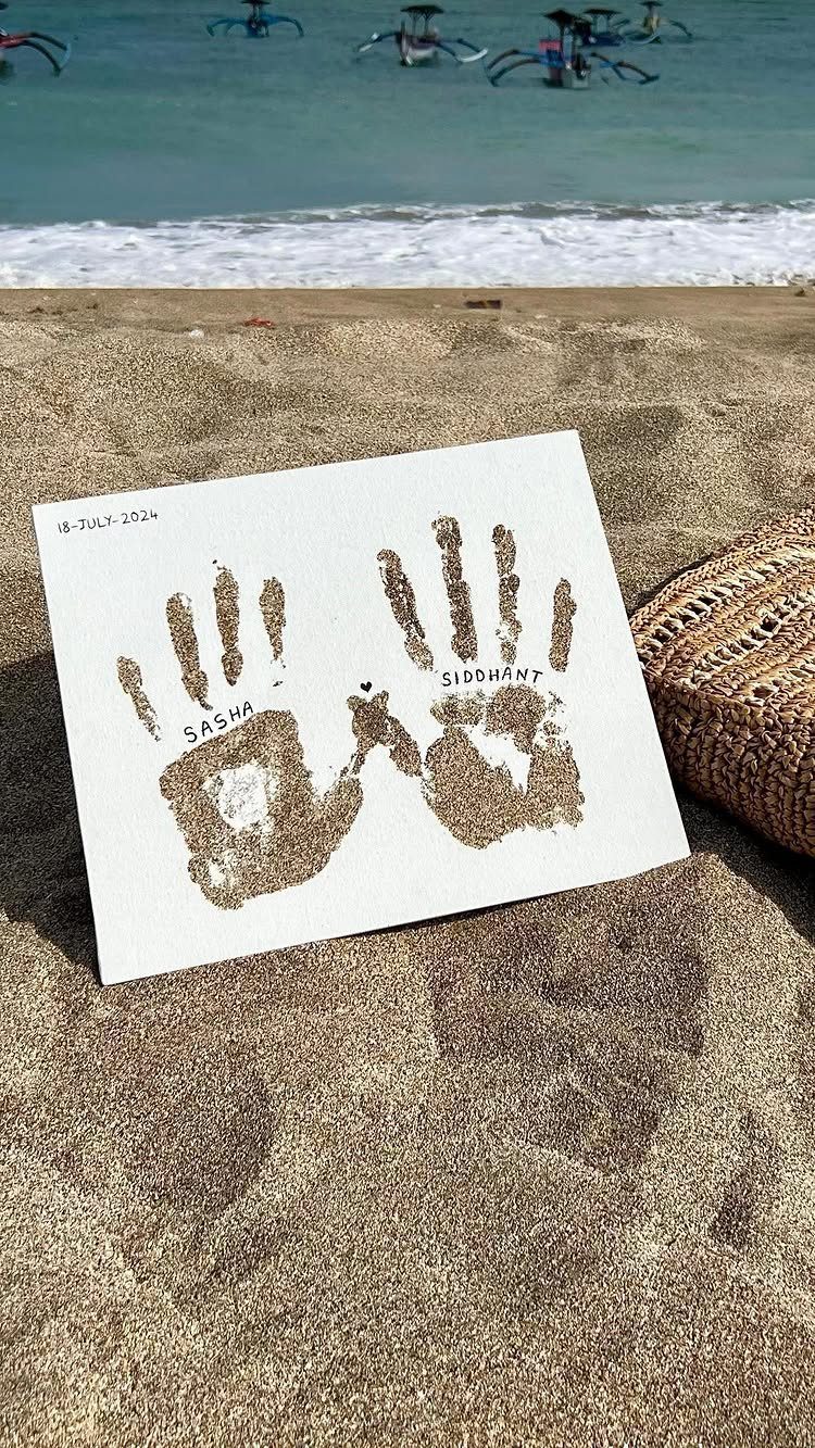 Sand handprints on a white paper resting on a beach with ocean background