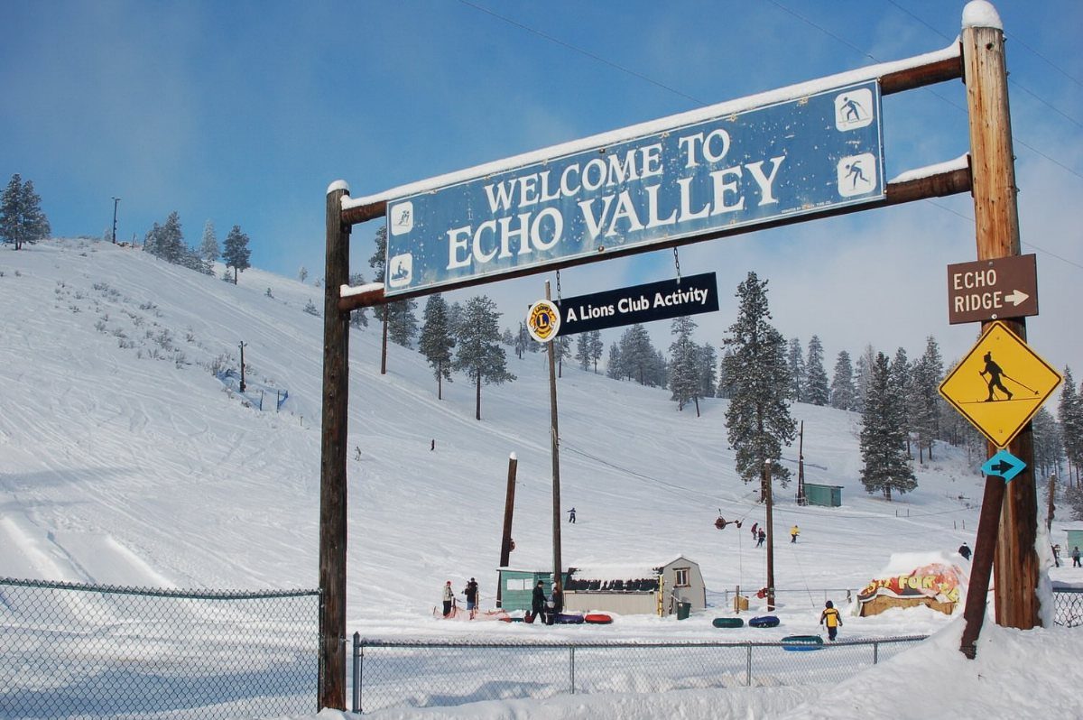 Welcome sign at Echo Valley ski resort with people tubing on snowy slopes