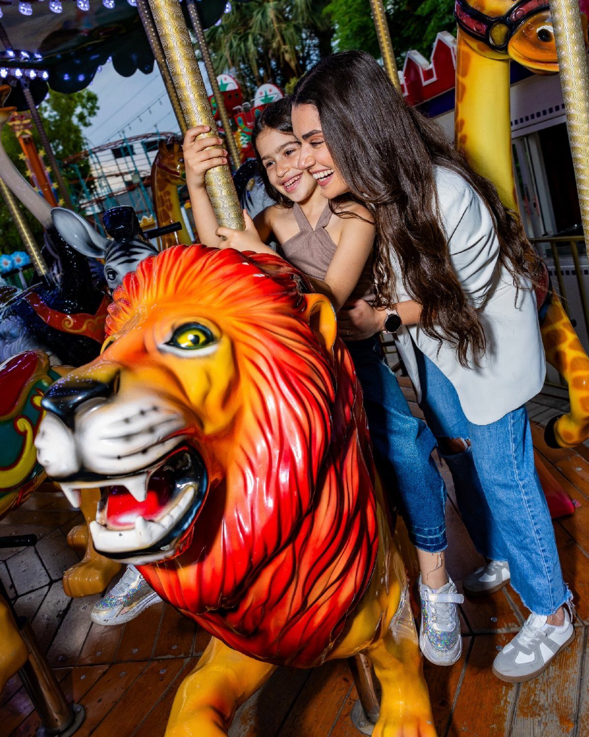 Woman and girl laughing while riding a colorful lion on a carousel ride.