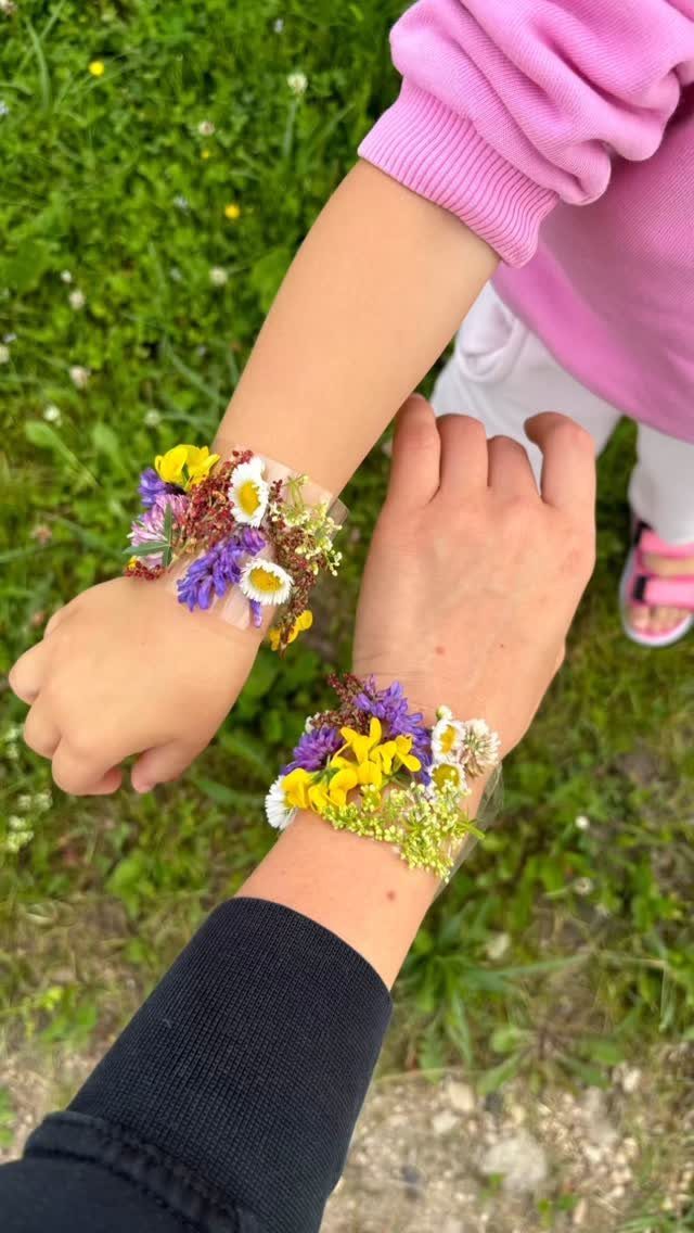 Two wrists wearing handmade bracelets made of clear tape and colorful wildflowers.