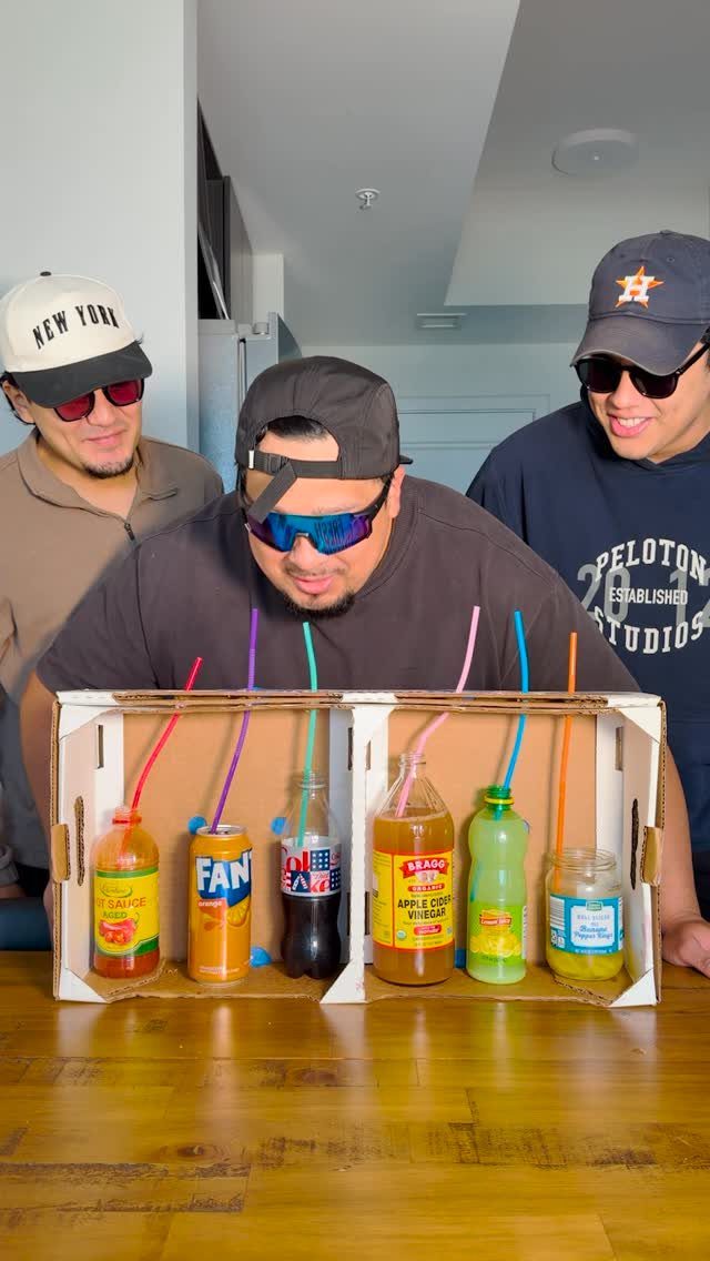 Three men playing a blind taste test game with colorful drinks and straws.