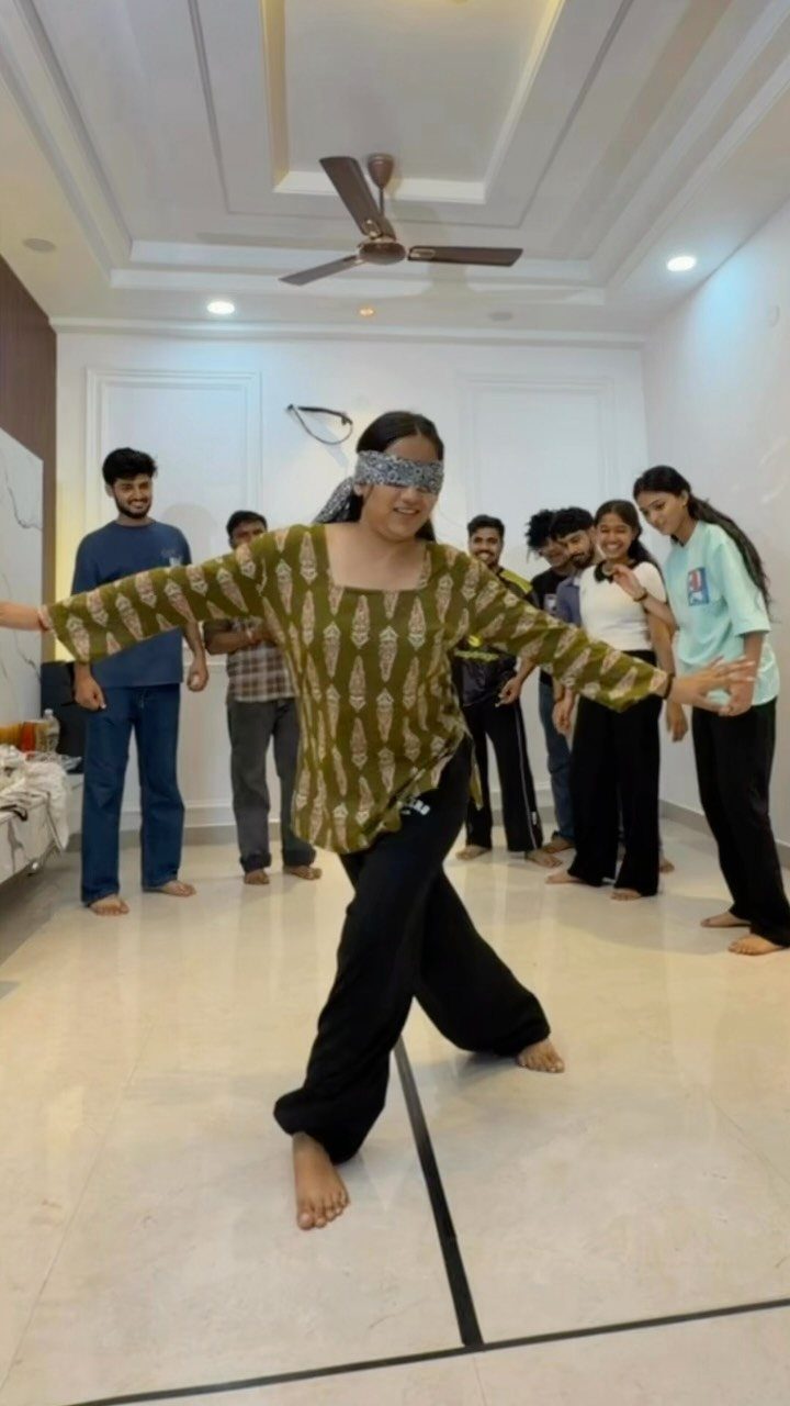 Blindfolded woman balancing on one leg while friends watch in a living room