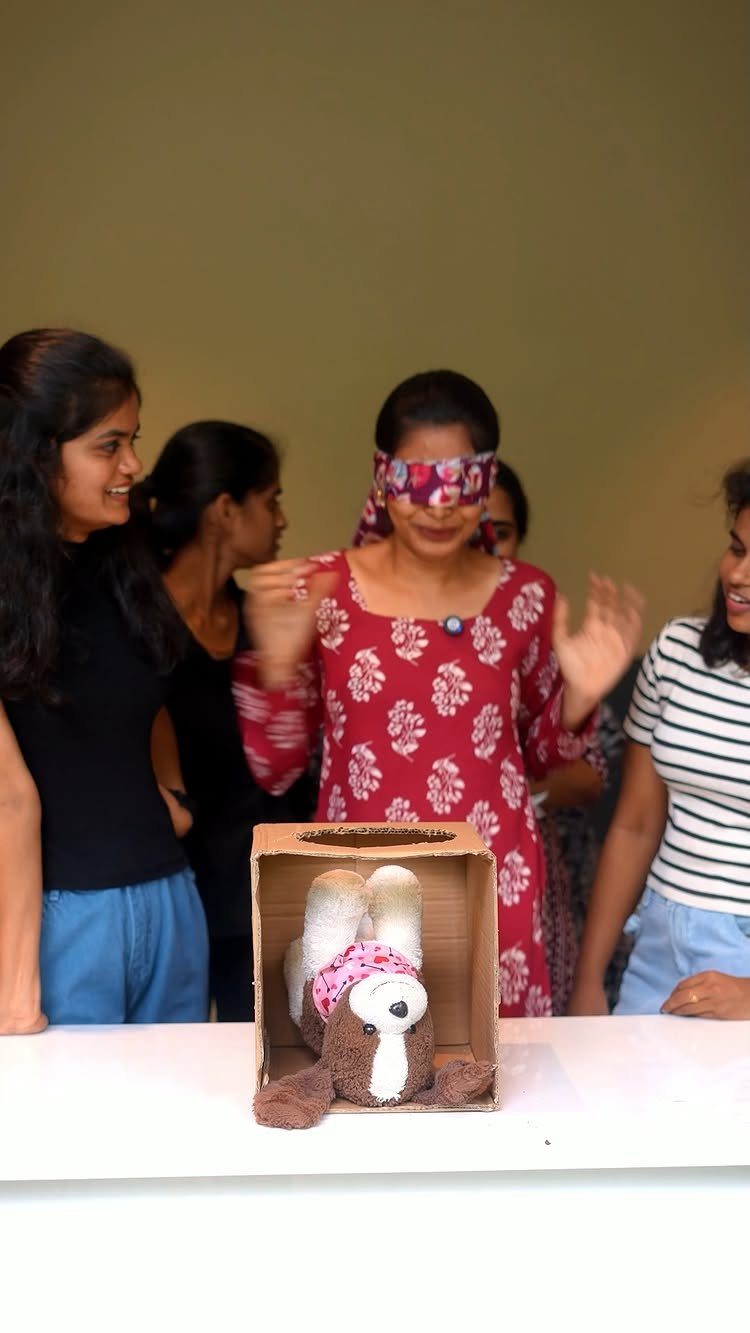 Blindfolded woman reacting to a plush toy inside a cardboard mystery box challenge.
