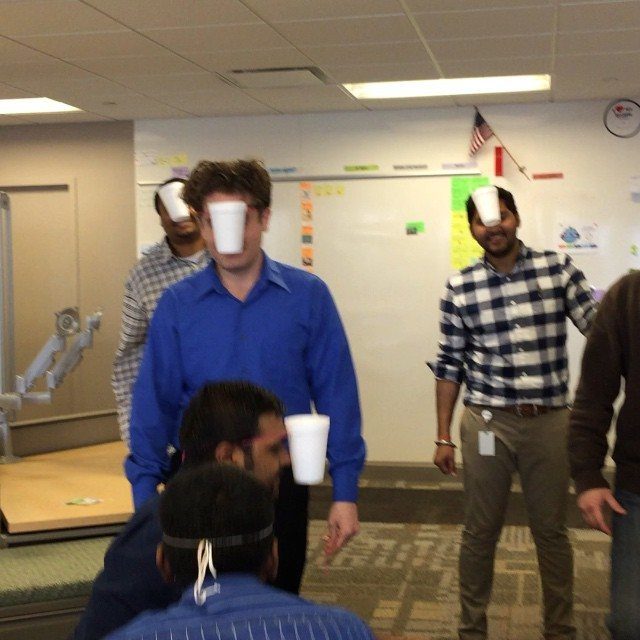 Men in an office wearing white plastic cups on their foreheads for a game.