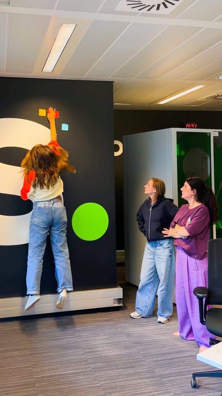 Woman jumping to place sticky notes on a wall while colleagues watch.