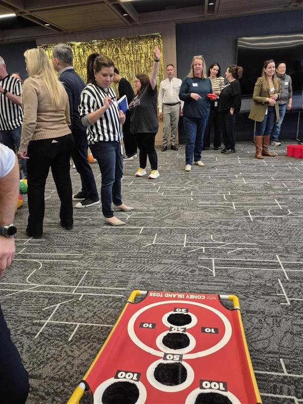Adults playing a bean bag toss game in a modern office setting.