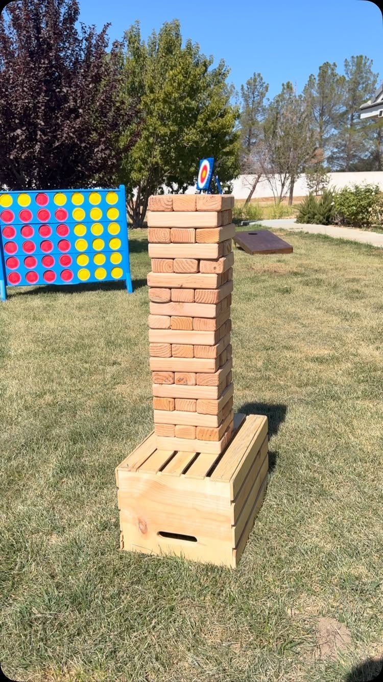 Giant Jenga wooden block tower standing on a crate in a sunny backyard.