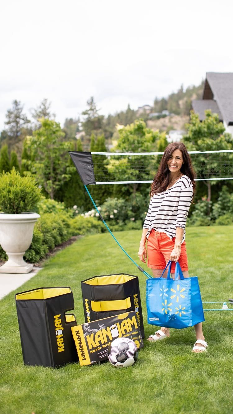 Woman standing on a lawn with KanJam bins, a soccer ball, and volleyball net.