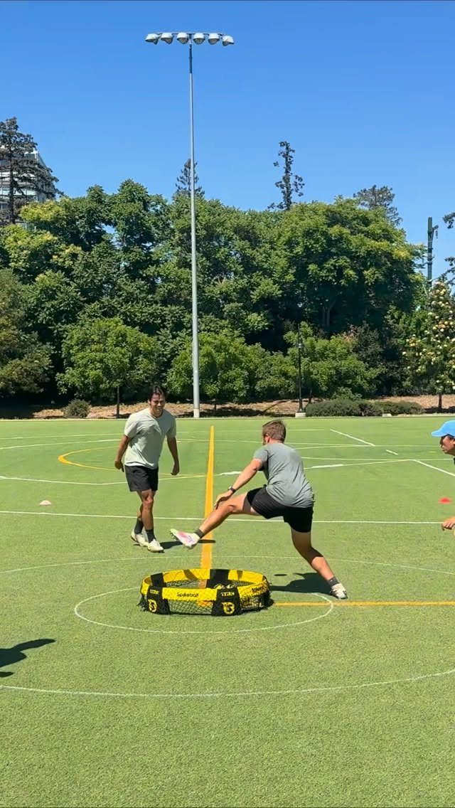 Two men playing Spikeball with a yellow net on a green turf field.