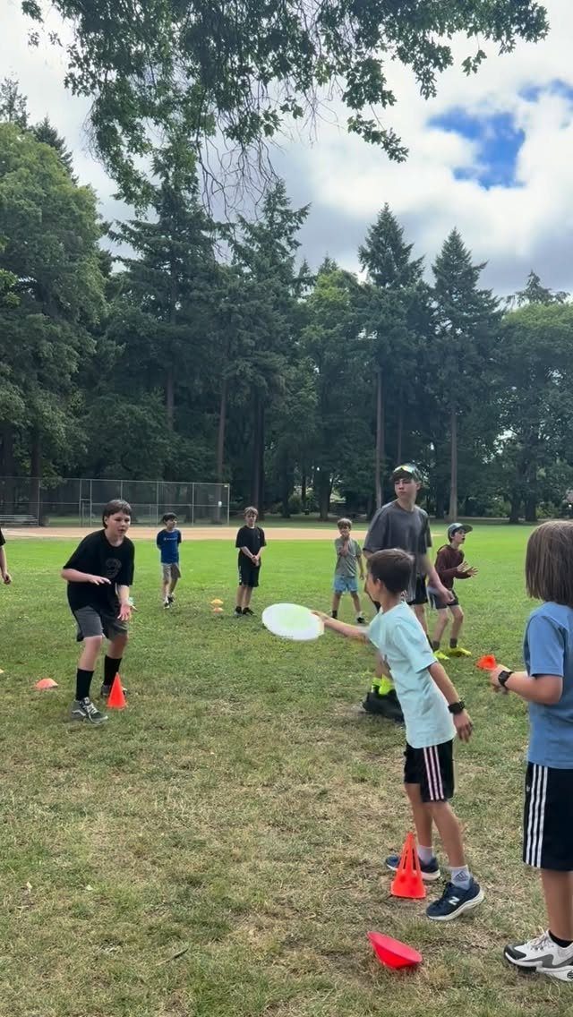 Children playing with a white frisbee on a grassy field with orange cones.