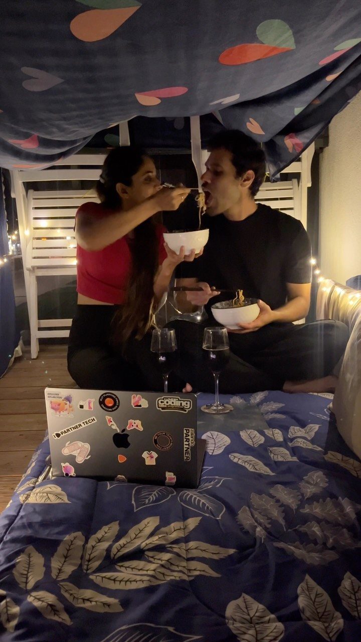 Couple eating and drinking wine inside a cozy blanket and pillow fort.