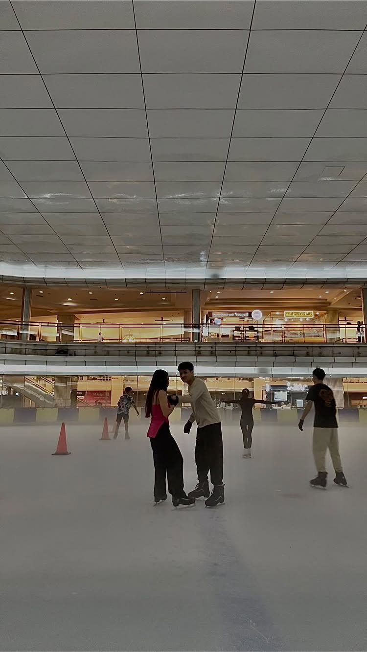 Couple ice skating together on an indoor rink in a shopping mall.