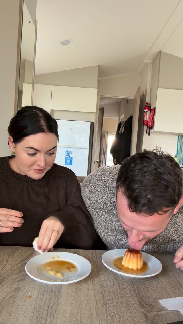 Man eating a caramel flan dessert without utensils while a woman watches.