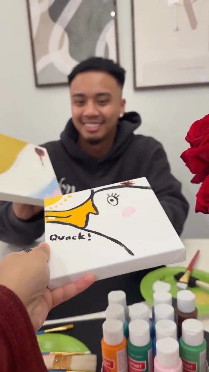 Man smiling behind a hand holding a funny duck painting during paint night.