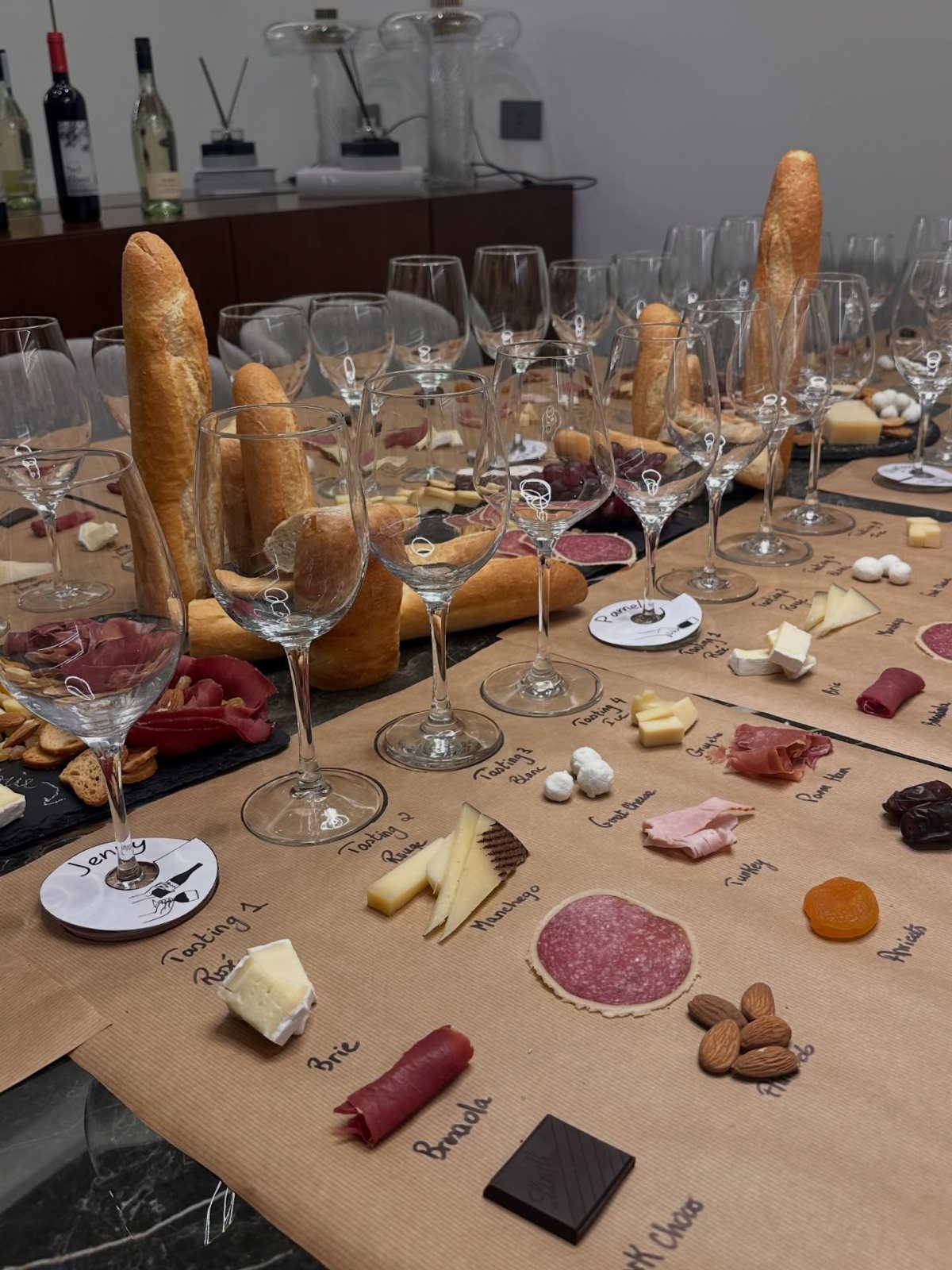 Wine and cheese tasting spread with meats, nuts, and baguettes on brown paper.