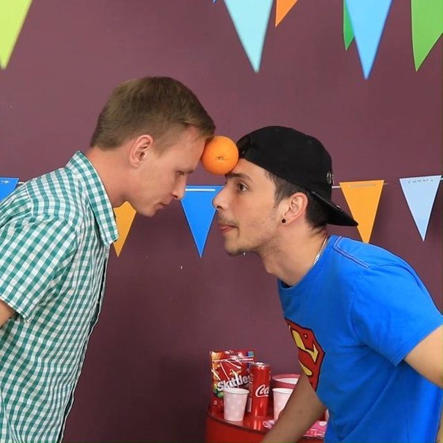 Two men balancing an orange between their foreheads during a party game challenge.