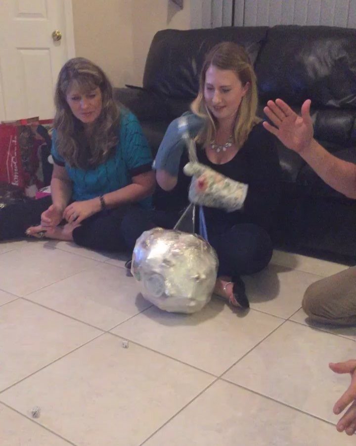 Two women playing a party game involving a foil-covered object and oven mitts.