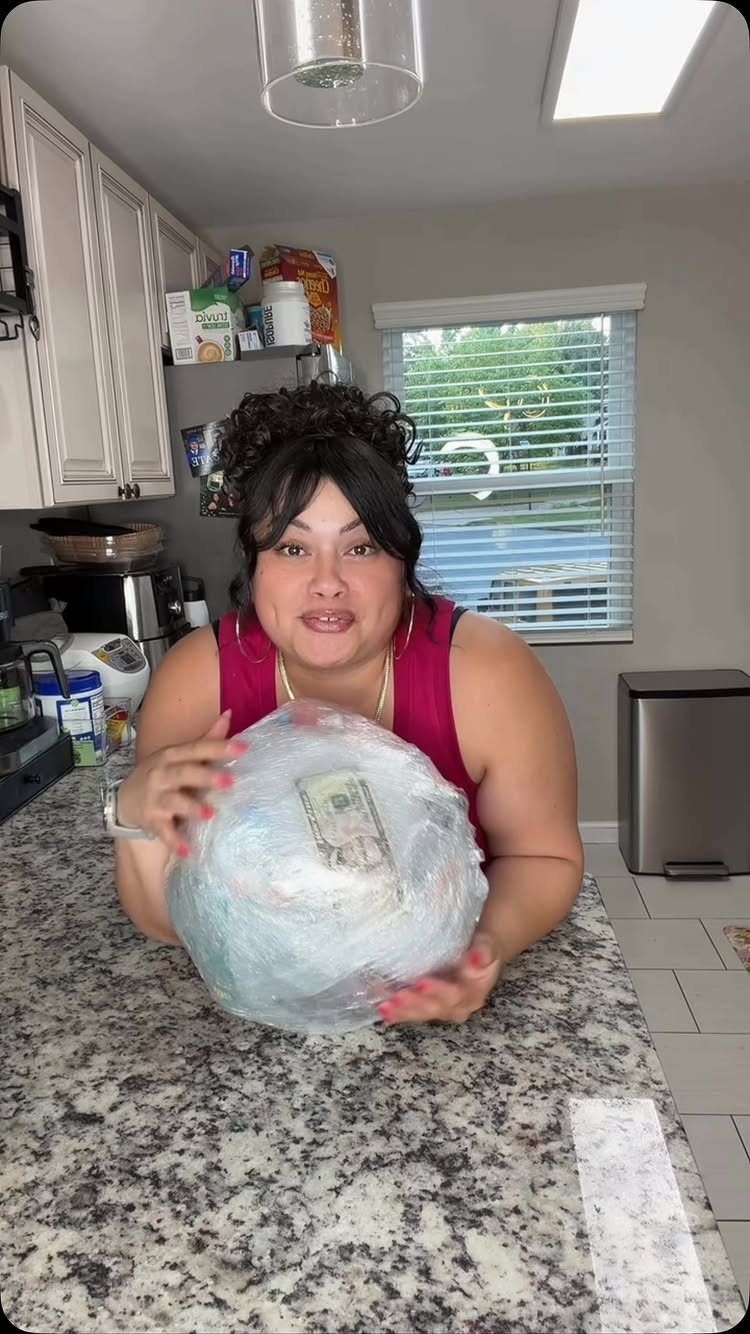 Woman holding a large plastic wrap ball with money inside in a kitchen