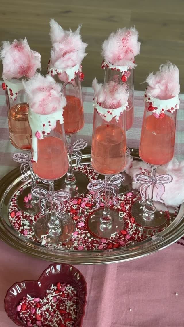Pink champagne flutes topped with cotton candy on a sprinkle-filled silver tray.