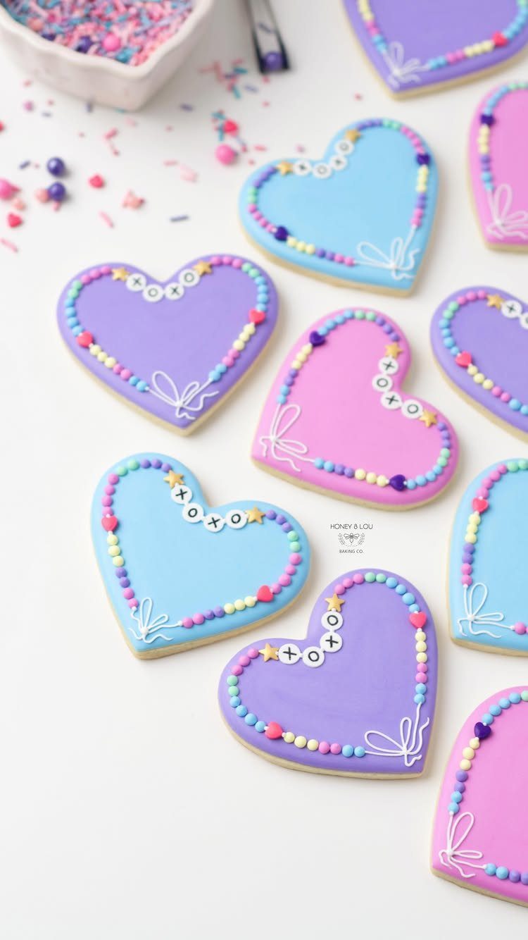 Heart-shaped cookies with purple, pink, and blue icing and colorful sprinkle decorations.