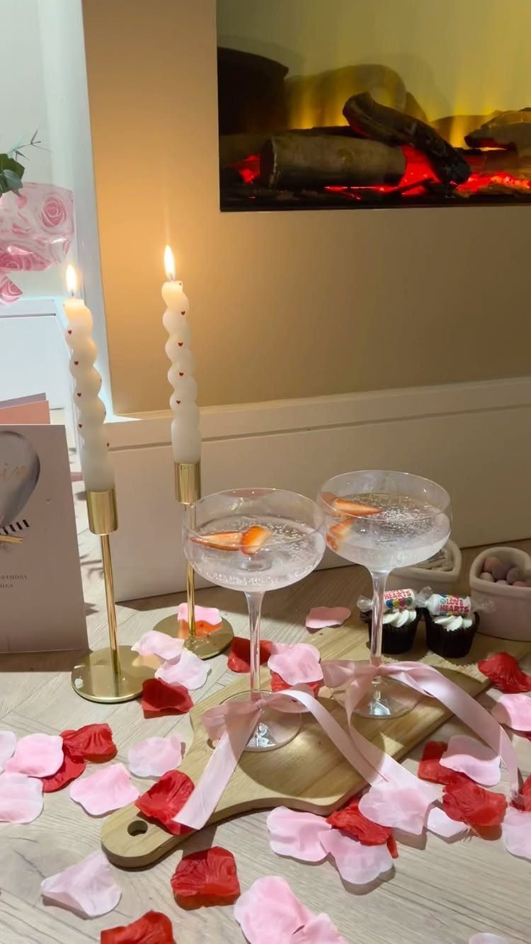 Sparkling drinks and twisted candles surrounded by rose petals near a warm fireplace.