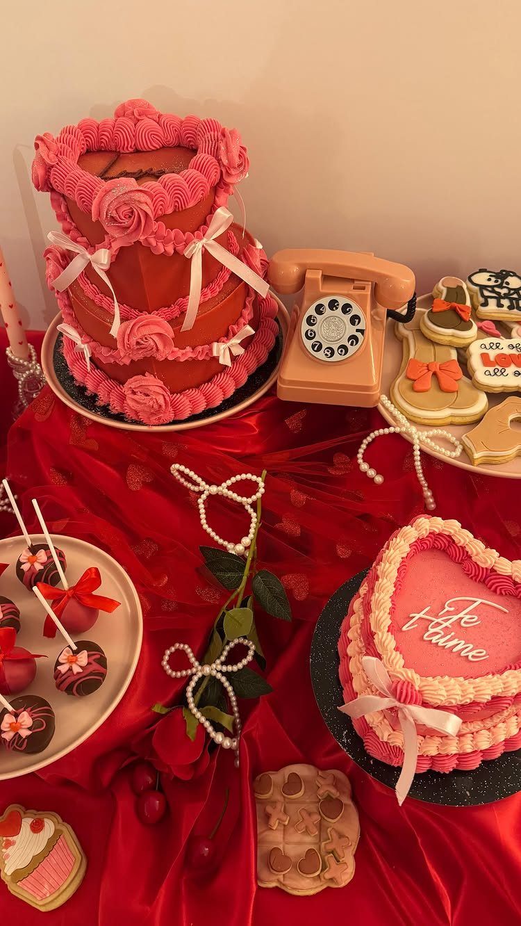 Pink cakes and decorated cookies on a red satin cloth with a vintage phone.