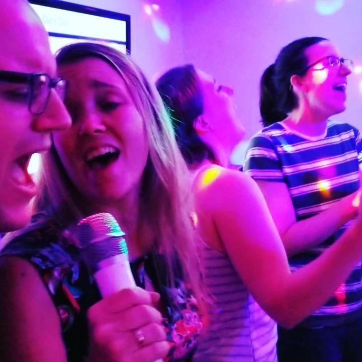 Group of friends singing into a microphone under purple party lights.