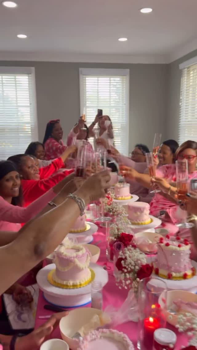 Women in pink clothing toast with champagne flutes at a brunch table with cakes.