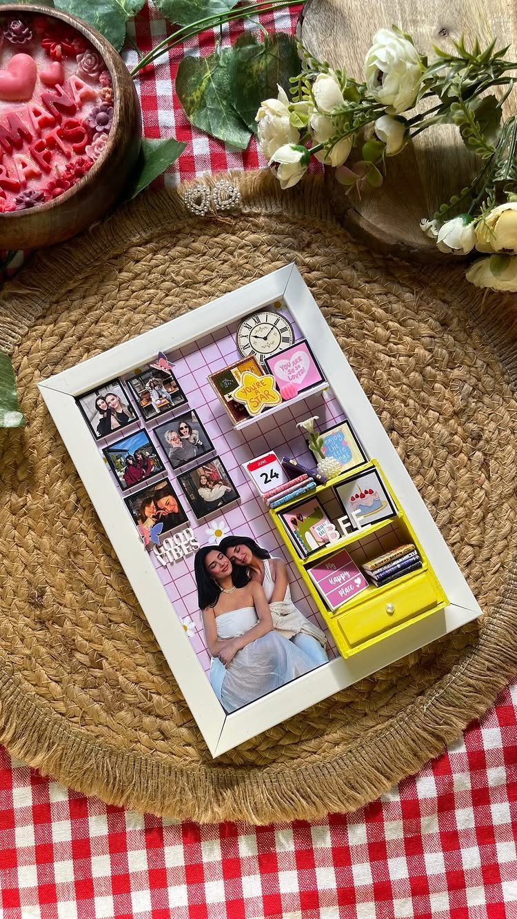 Miniature memory box with small photos and furniture inside a white shadow frame.