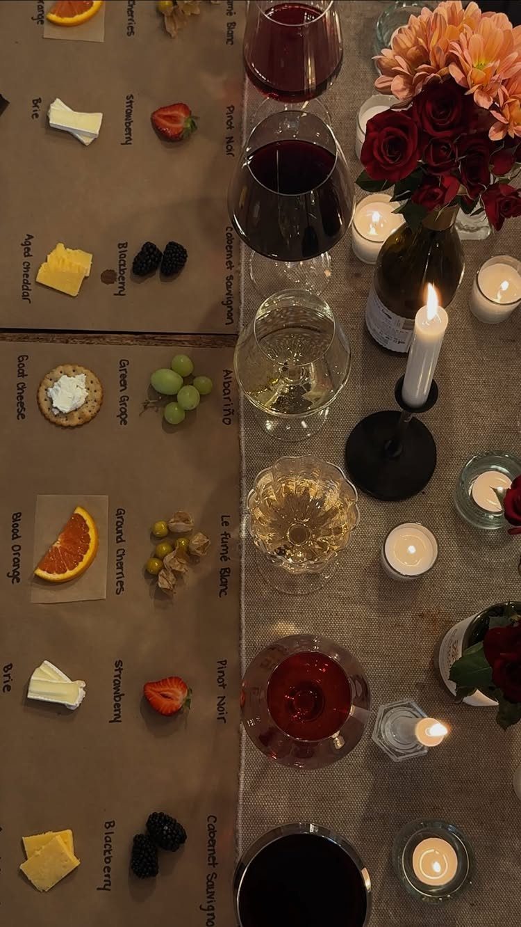 Wine tasting setup with glasses, cheese, fruit, and candles on a burlap table runner.