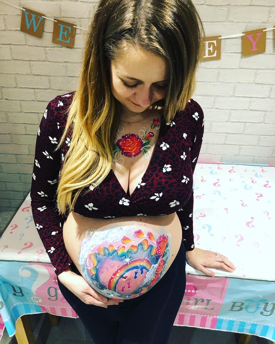 Pregnant woman with a colorful rainbow painted on her belly at a party.