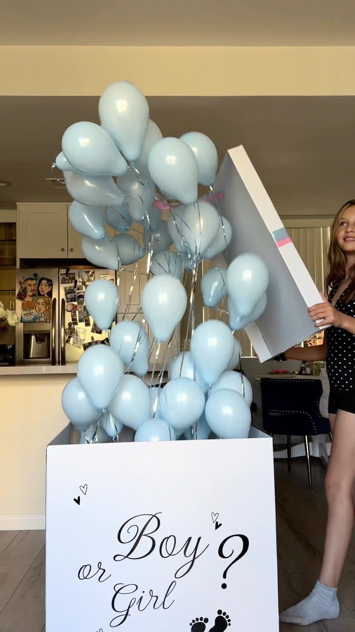Woman opening a white reveal box releasing light blue balloons in a kitchen